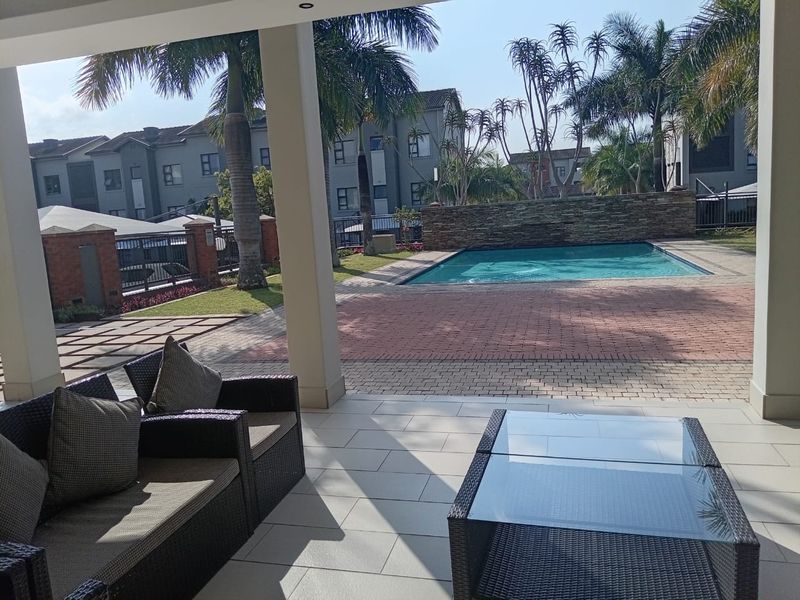 A spacious covered patio overlooking a private swimming pool and landscaped garden area within a residential apartment complex.