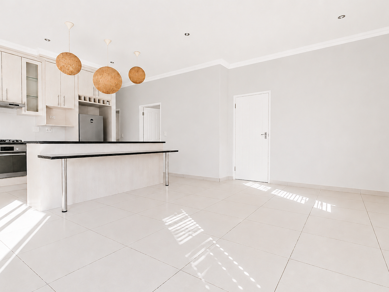Bright open-plan kitchen and living area featuring light-toned cabinetry, a breakfast bar, integrated appliances, and neutral tiled flooring throughout.