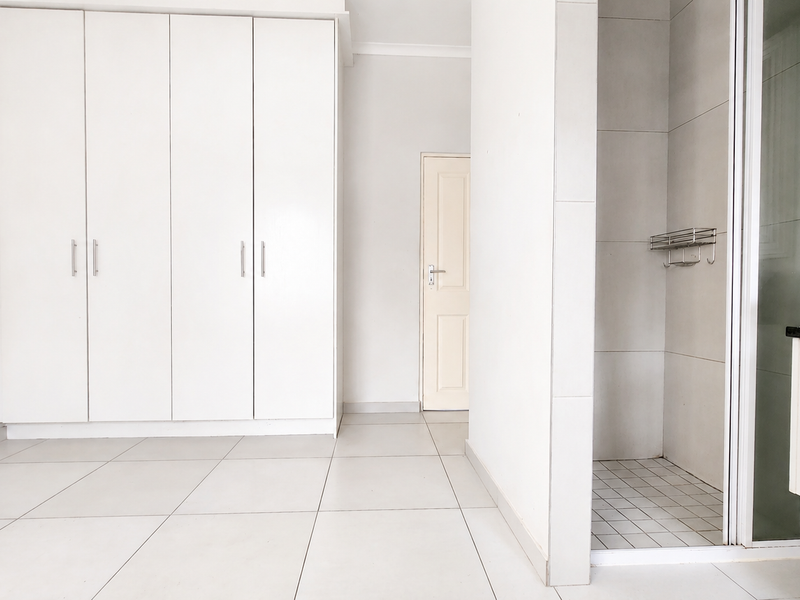 A bright, empty bedroom featuring built-in wardrobes, tiled flooring, and an en-suite shower area with a modern vanity and vessel sink.
