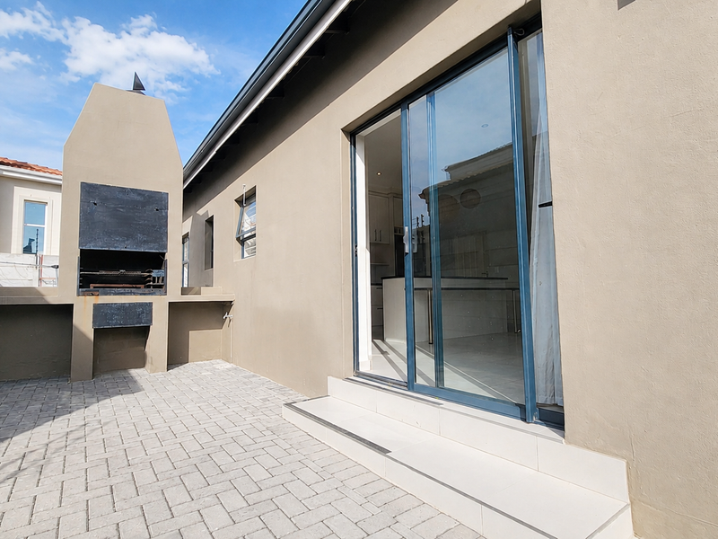 A clean outdoor patio area featuring a built-in braai, paved flooring, and sliding glass doors providing access to the interior living space.