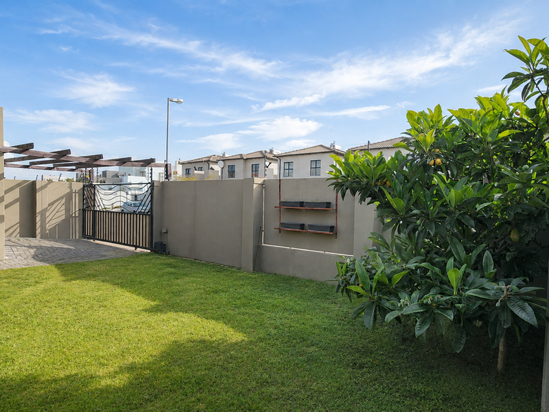 A well-maintained rear garden featuring a paved patio area with a timber pergola, enclosed by boundary walls and a metal gate.