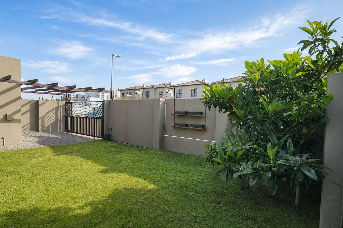 A well-maintained rear garden featuring a paved patio area with a timber pergola, enclosed by boundary walls and a metal gate.