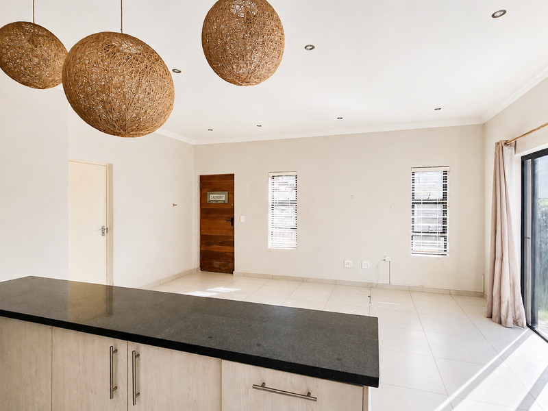 Spacious open-plan living area featuring a modern kitchen island with stone countertops, tiled flooring, and large sliding doors leading to the exterior.