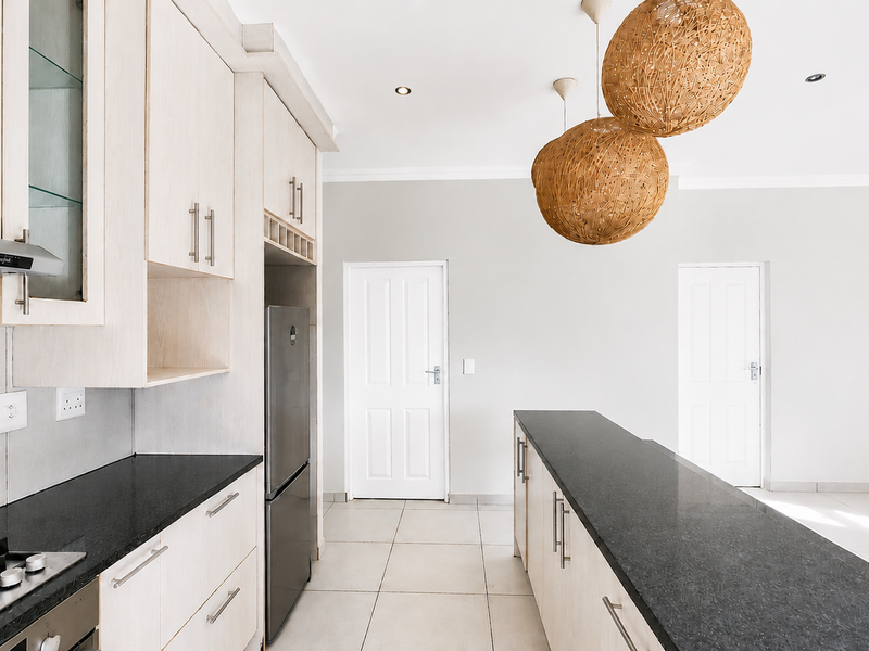 Modern kitchen featuring light wood cabinetry, dark granite countertops, a gas hob, and a central island, finished with neutral tiled flooring.
