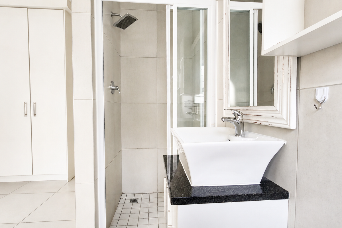 A clean, modern bathroom featuring a glass-enclosed shower, a vessel sink on a granite vanity, and ample built-in cupboard storage.