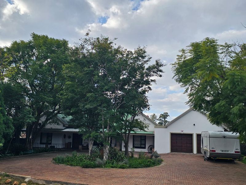 Front elevation of a residential property featuring a paved circular driveway, established garden, and an attached double garage.