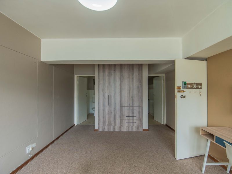 A spacious bedroom featuring neutral wall tones, carpeted flooring, and modern built-in cupboards with ample storage space.