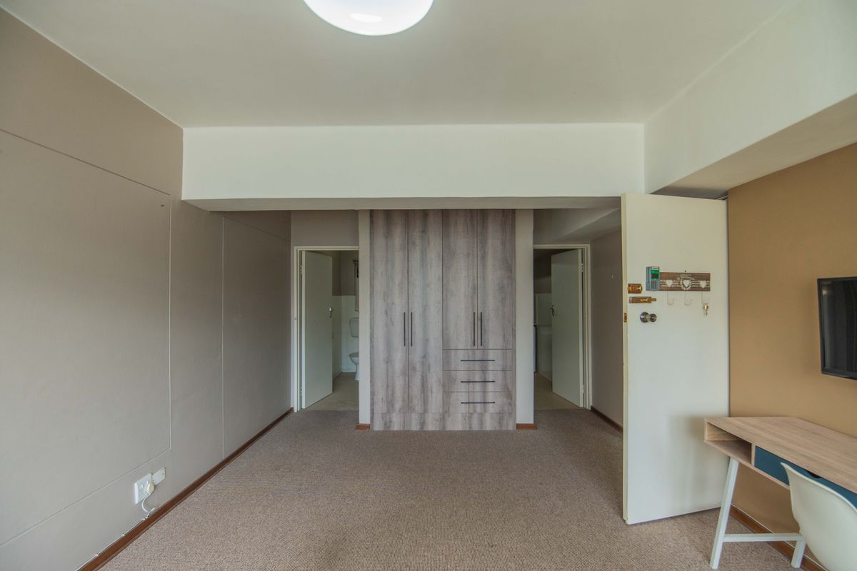 A spacious bedroom featuring neutral wall tones, carpeted flooring, and modern built-in cupboards with ample storage space.