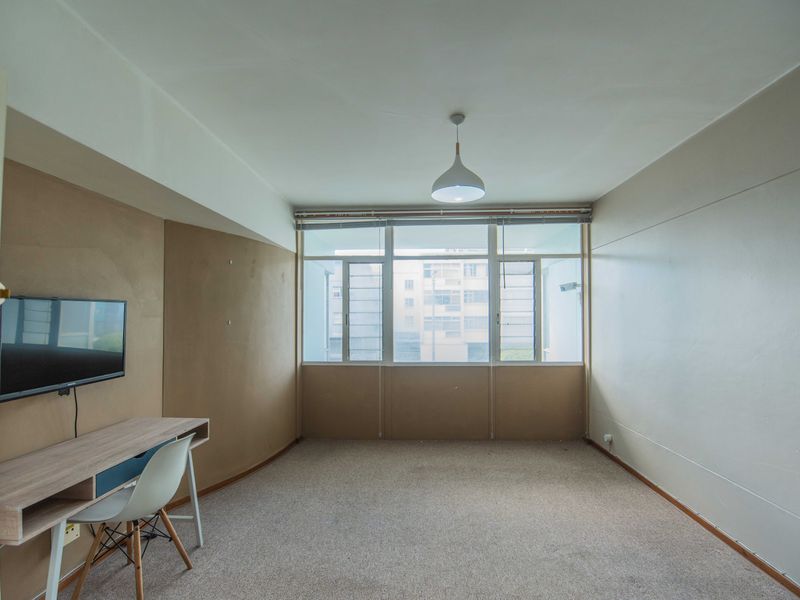 A spacious, sunlit living area featuring large windows, neutral wall tones, and carpet flooring, offering a blank canvas for personalization.