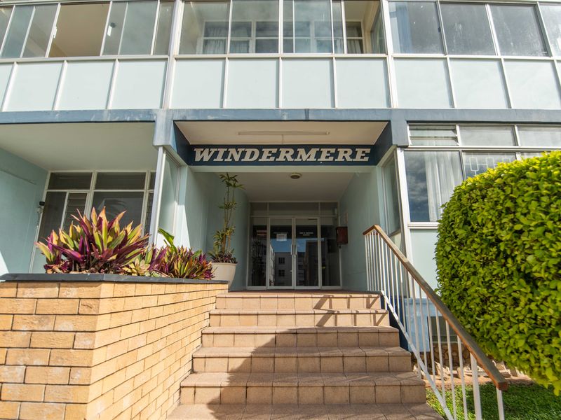 The front entrance of Windermere apartment complex featuring tiled steps, a brick retaining wall, and a secure glass door entry.