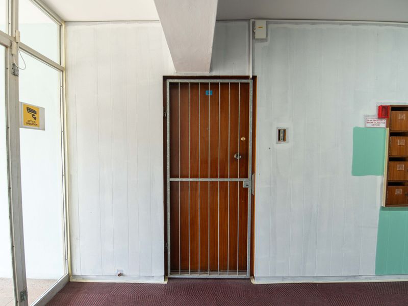 Apartment entrance area featuring a wooden door with a security gate, wall-mounted mailboxes, and an emergency key access point.