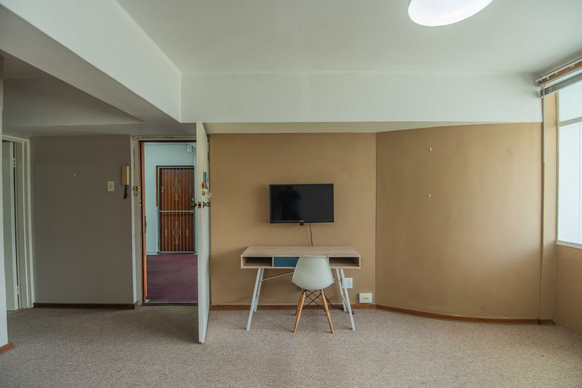 A sparsely furnished living area featuring carpeted flooring, neutral wall tones, and an integrated intercom system near the entrance.