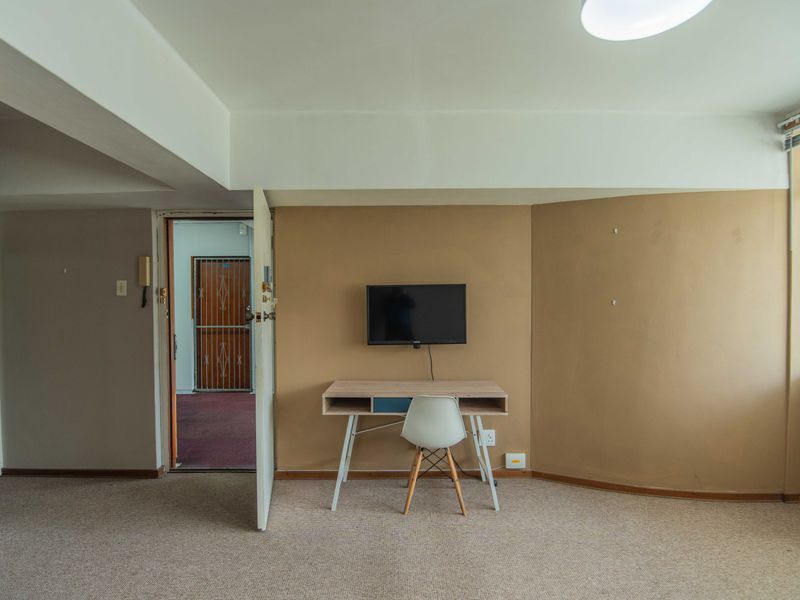 A sparsely furnished living area featuring carpeted flooring, neutral wall tones, and an integrated intercom system near the entrance.