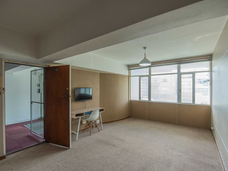 An empty living room featuring large windows, carpet flooring, and a security gate at the entrance, offering a blank canvas for potential renovation.