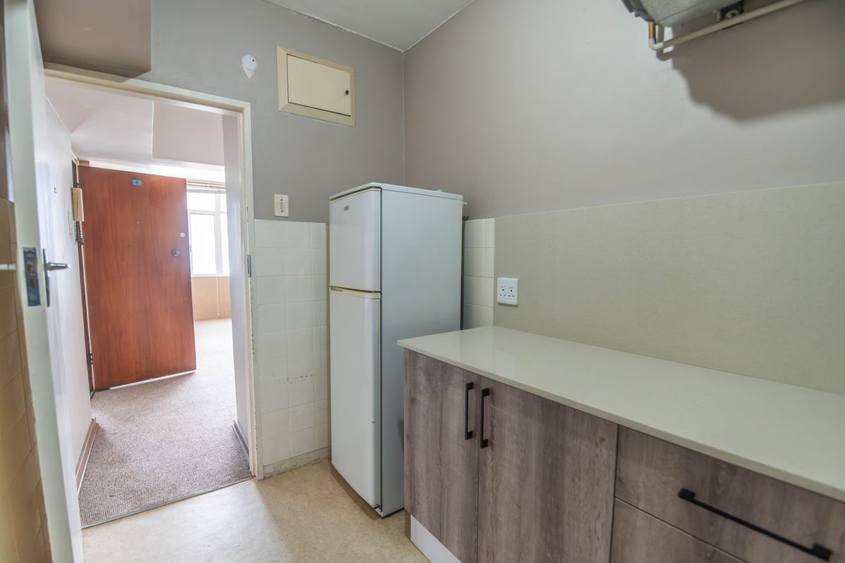 A functional kitchen area featuring modern wood-look cabinetry, a neutral countertop, and tiled splashback, with direct access to the main living space.