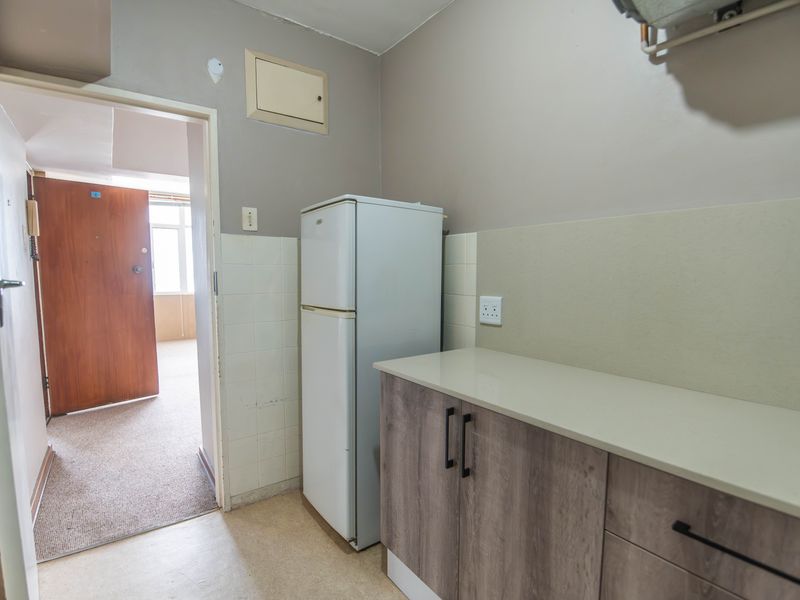A functional kitchen area featuring modern wood-look cabinetry, a neutral countertop, and tiled splashback, with direct access to the main living space.