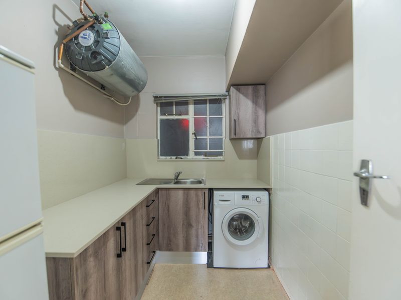 Functional laundry area featuring built-in cabinetry, a stainless steel sink, tiled splashback, and a wall-mounted geyser unit.