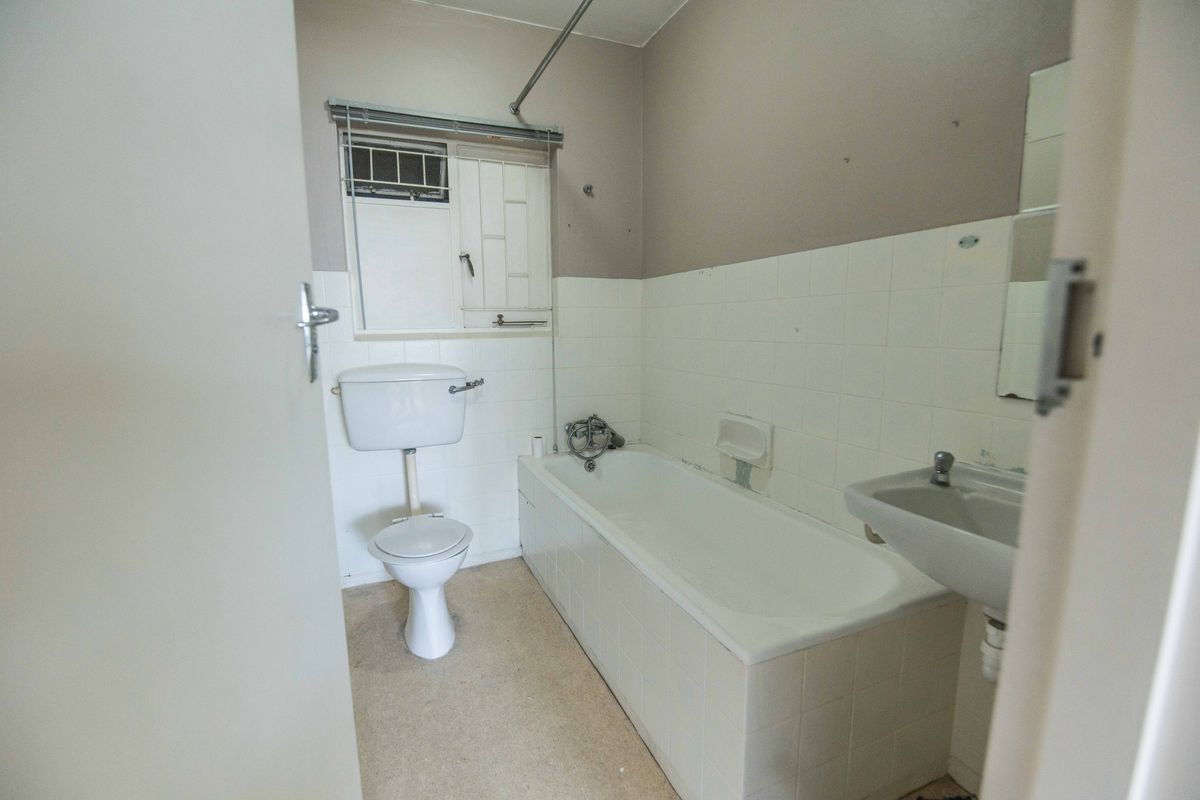 A dated bathroom featuring a standard bathtub, toilet, and wall-mounted basin with tiled splashbacks and a security window grille.