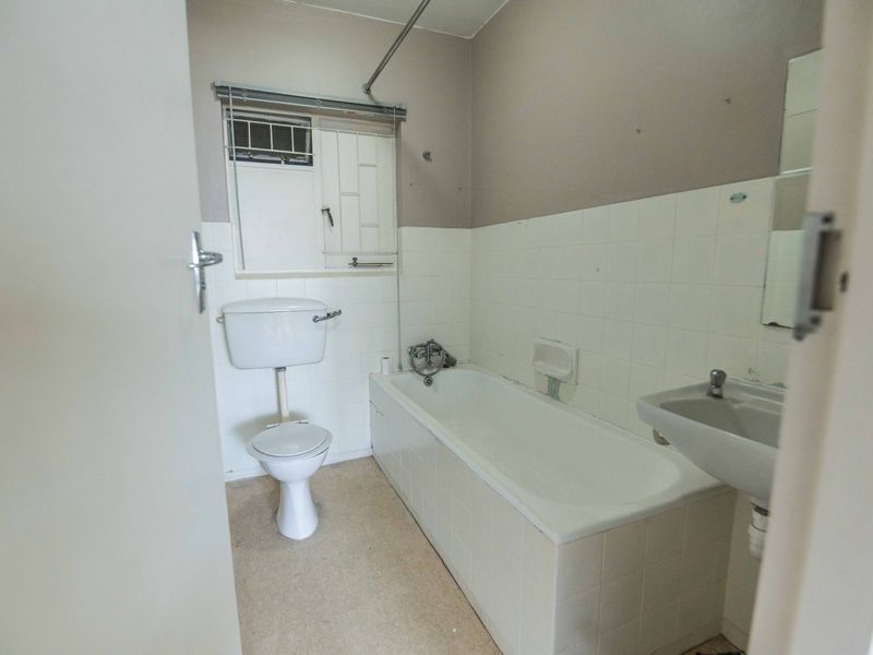 A dated bathroom featuring a standard bathtub, toilet, and wall-mounted basin with tiled splashbacks and a security window grille.