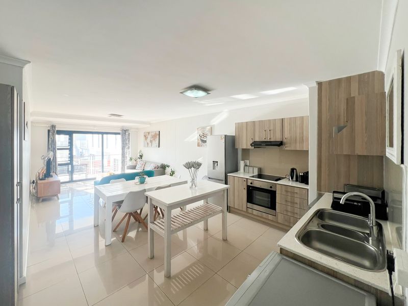 Bright open-plan living area featuring a modern kitchen with wood-finish cabinetry, integrated appliances, and seamless flow to a balcony through sliding glass doors.