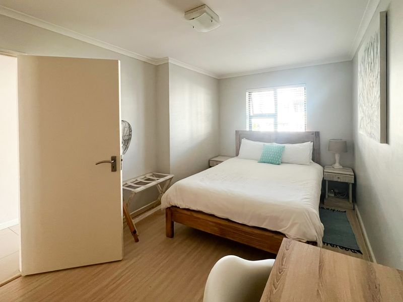 A functional bedroom featuring light-toned laminate flooring, neutral wall finishes, and a window with fitted blinds, providing a clean and simple living space.