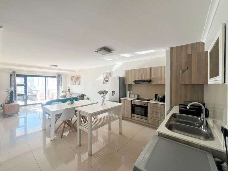 Modern open-plan apartment featuring a contemporary kitchen with built-in cabinetry, integrated appliances, and seamless flow to the living area and balcony.
