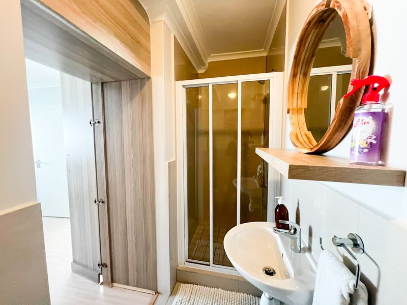 A functional bathroom featuring a shower enclosure, pedestal basin with chrome fixtures, and built-in cabinetry, presenting a clean and well-maintained space.