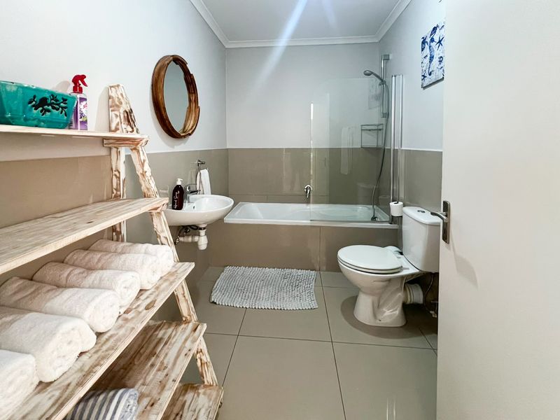 A functional bathroom featuring a bathtub with a glass shower screen, a wall-mounted basin, and a standard toilet with neutral tiled finishes.
