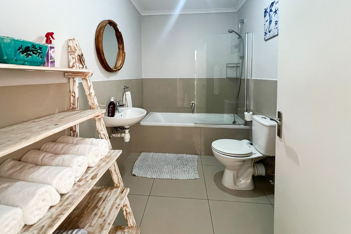A functional bathroom featuring a bathtub with a glass shower screen, a wall-mounted basin, and a standard toilet with neutral tiled finishes.
