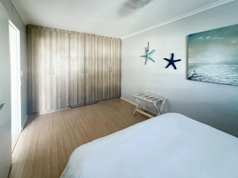 A well-maintained bedroom featuring light wood-tone laminate flooring and extensive floor-to-ceiling built-in cupboards providing ample storage space.