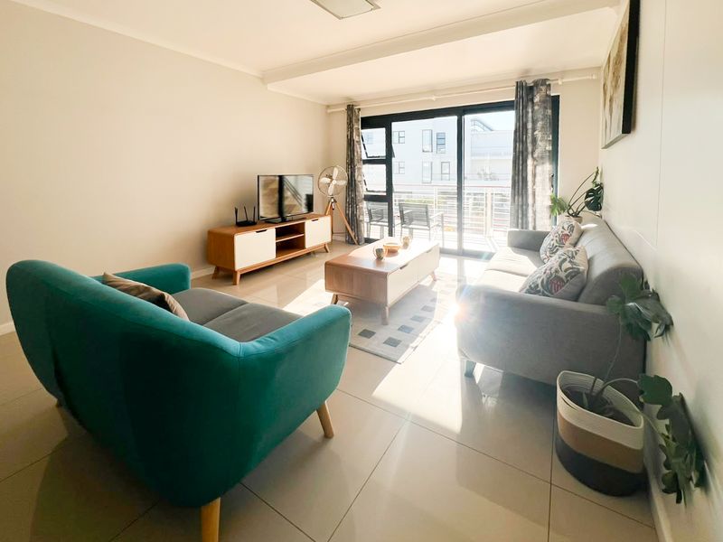 A bright and well-maintained living room featuring large format floor tiles and a sliding glass door providing access to the balcony.
