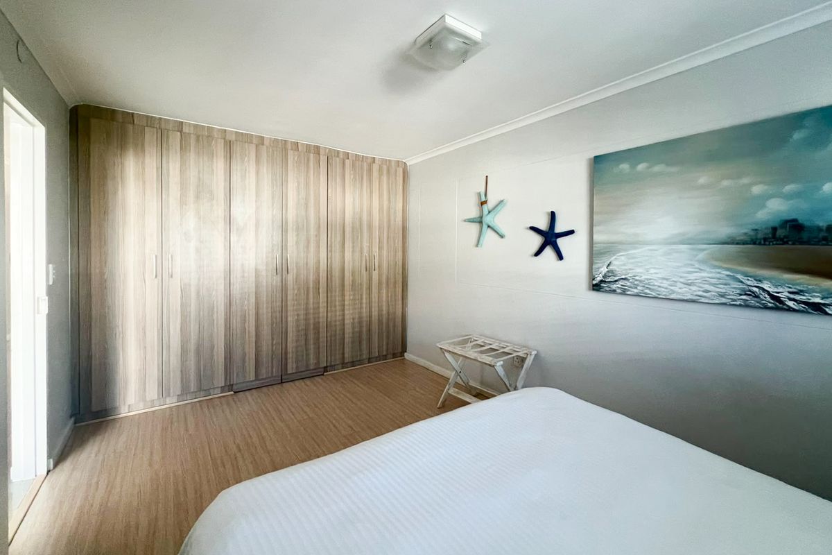 A well-maintained bedroom featuring light wood-tone laminate flooring and extensive floor-to-ceiling built-in cupboards providing ample storage space.