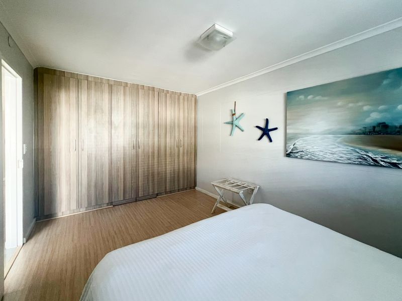 A well-maintained bedroom featuring light wood-tone laminate flooring and extensive floor-to-ceiling built-in cupboards providing ample storage space.
