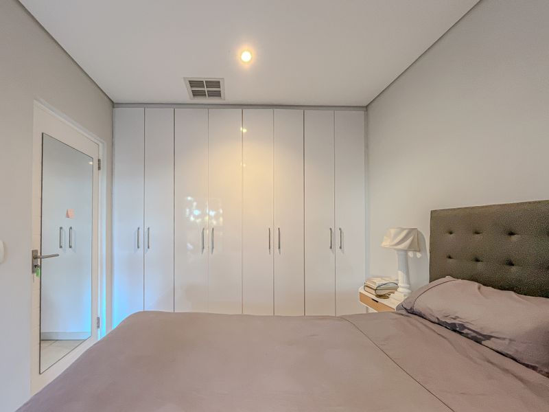 A well-maintained bedroom featuring floor-to-ceiling white built-in cupboards, recessed lighting, and a mirrored door, offering a clean and modern aesthetic.