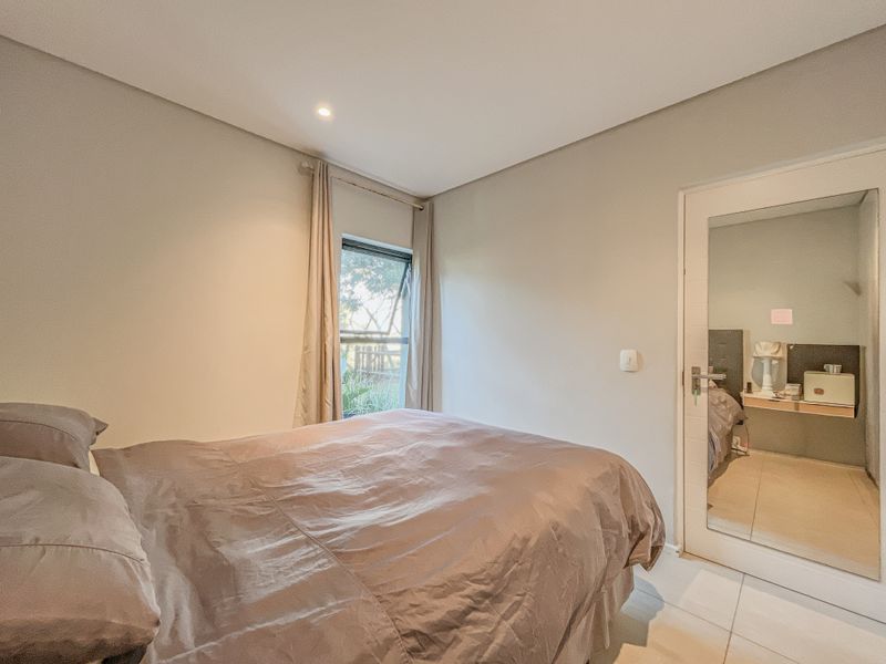 A well-lit bedroom featuring tiled flooring, a casement window, and a mirrored door leading to an adjacent space.
