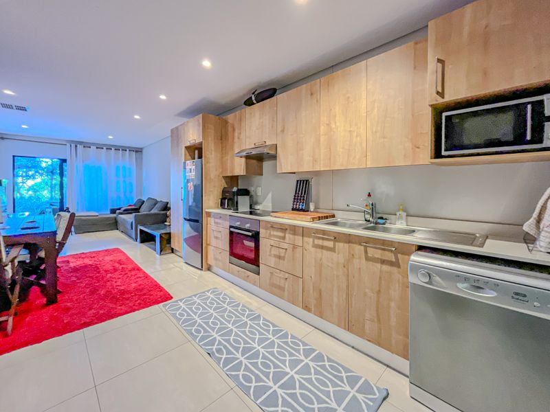 Open-plan living area featuring a modern kitchen with light wood cabinetry, built-in appliances, and tiled flooring, seamlessly flowing into the adjacent dining and lounge space.
