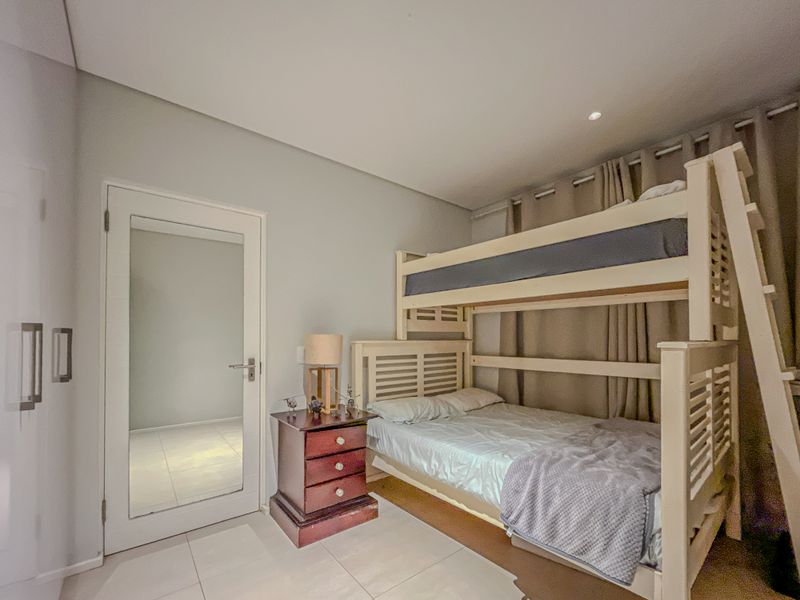 A well-maintained bedroom featuring neutral wall tones, tiled flooring, and recessed ceiling lighting, providing a clean and functional living space.
