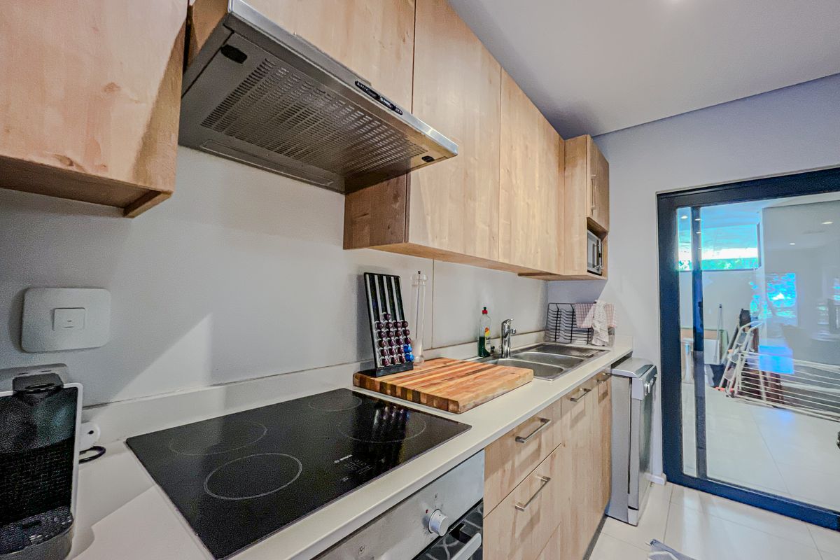 Modern kitchen featuring light wood cabinetry, stone countertops, integrated electric hob, oven, and extractor fan, with direct access to an outdoor patio area.