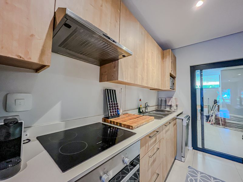 Modern kitchen featuring light wood cabinetry, stone countertops, integrated electric hob, oven, and extractor fan, with direct access to an outdoor patio area.