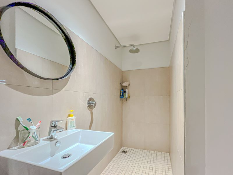 Modern bathroom featuring a wall-mounted basin, chrome fixtures, and a walk-in shower with neutral wall tiling.