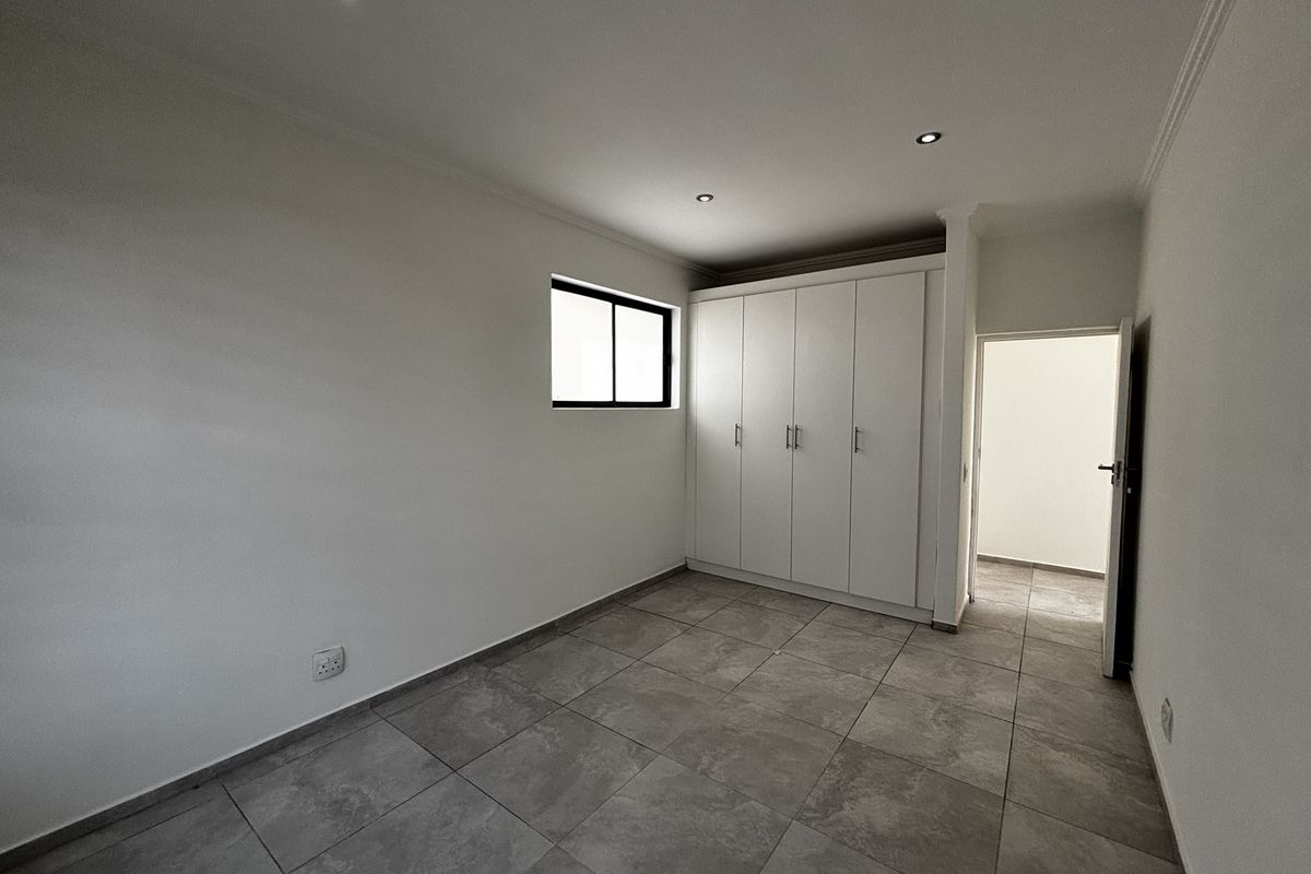 A clean, empty bedroom featuring neutral tiled flooring, built-in cupboards, and modern recessed downlighting, offering a blank canvas for personalization.