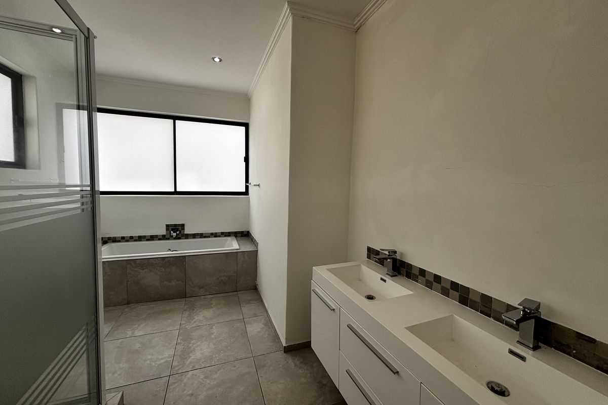 Modern bathroom featuring a double vanity, built-in bathtub, and a separate shower enclosure with neutral floor tiling and mosaic accents.