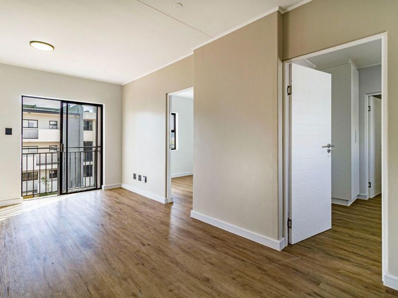 An empty, well-lit living area featuring modern laminate flooring, neutral walls, and a sliding door leading to a private balcony.