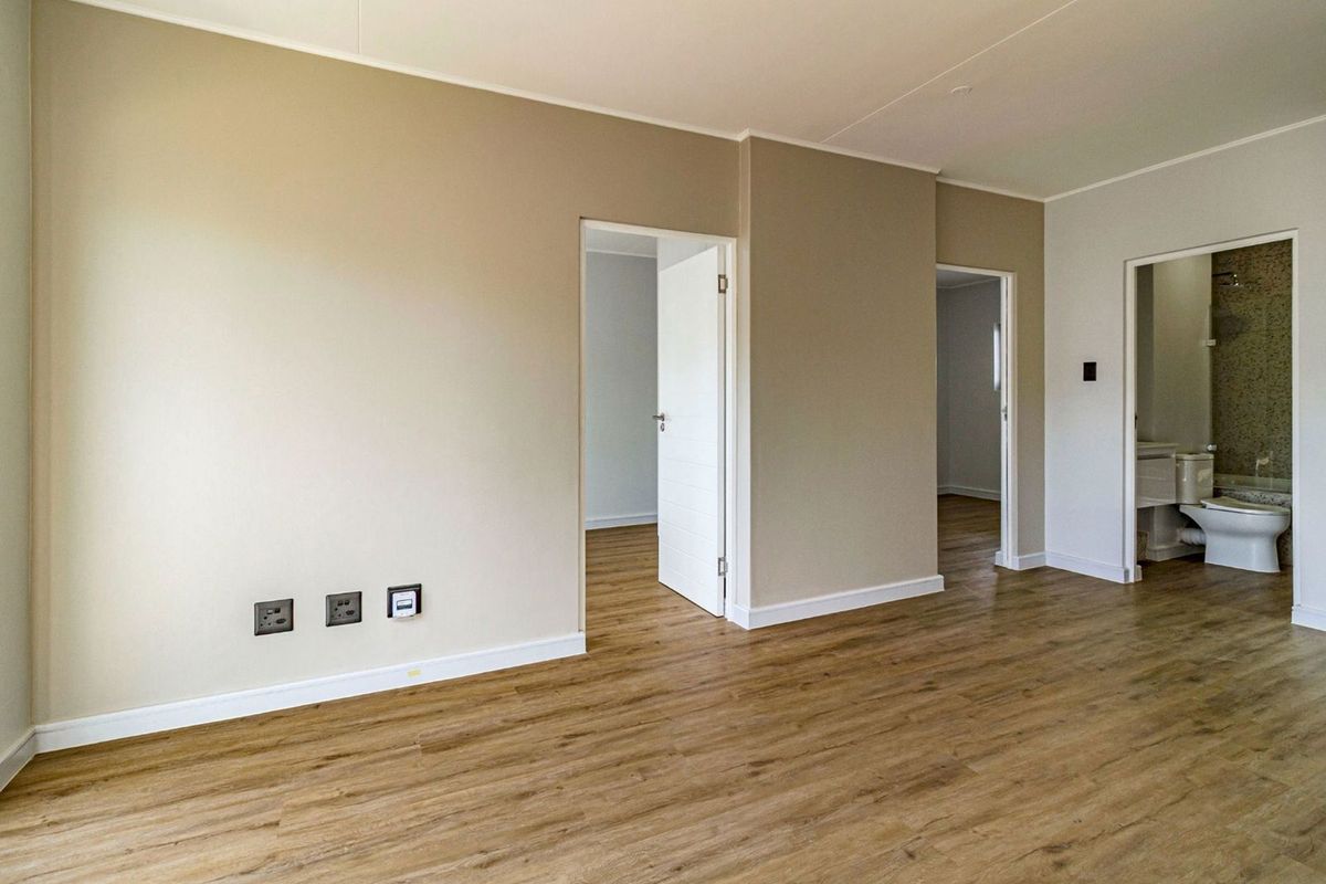 An empty, well-maintained living area featuring modern laminate flooring, neutral wall tones, and direct access to adjacent rooms and a bathroom.