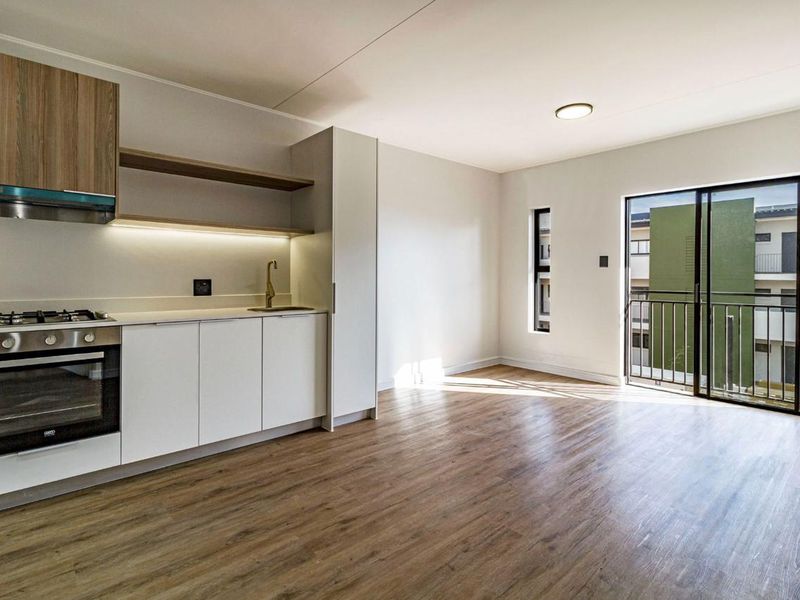 Modern open-plan kitchen and living area featuring sleek cabinetry, built-in appliances, laminate flooring, and direct access to a private balcony.