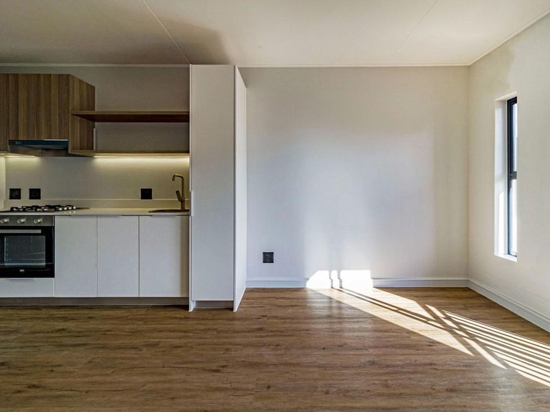Modern open-plan kitchen featuring sleek white cabinetry, wood-tone shelving, integrated appliances, and durable laminate flooring in a bright, sunlit space.