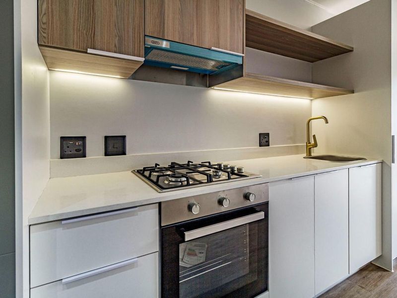Modern kitchen featuring stone countertops, gas hob, built-in oven, brass faucet, and sleek cabinetry with integrated under-cabinet lighting.