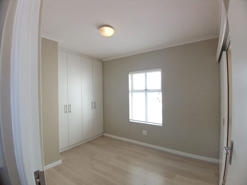A clean, empty bedroom featuring neutral walls, light laminate flooring, and ample built-in cupboard storage.