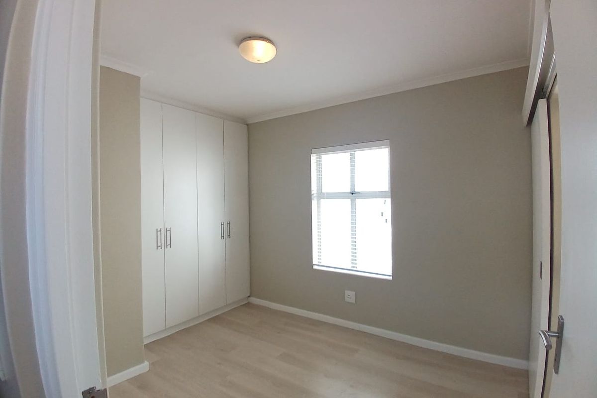 A clean, empty bedroom featuring neutral walls, light laminate flooring, and ample built-in cupboard storage.