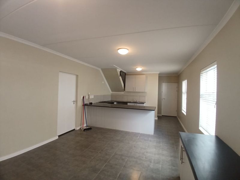 An open-plan living and kitchen area featuring tiled flooring, neutral walls, built-in kitchen cabinetry with countertops, and a staircase.